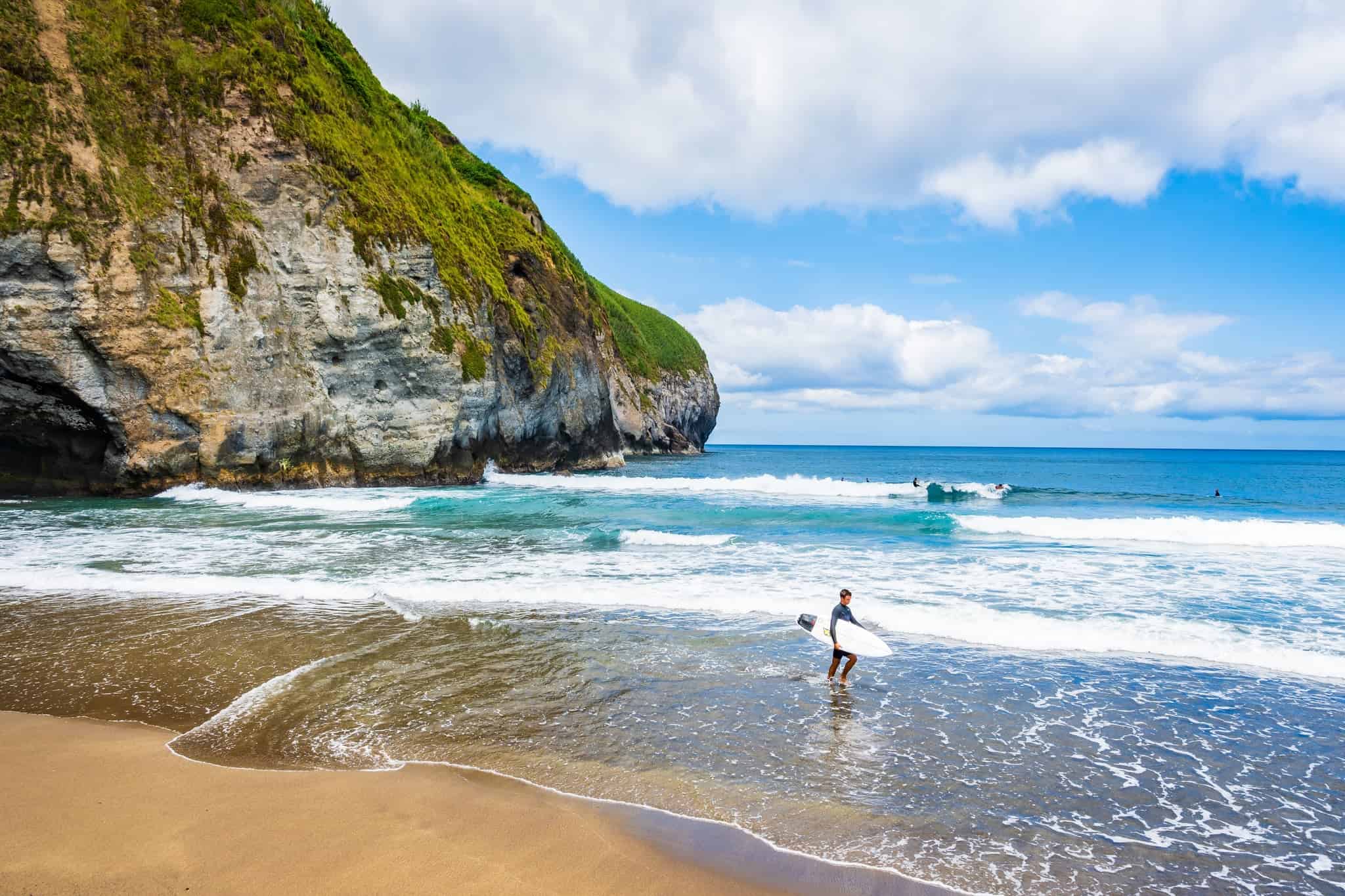 Surfař s deskou vstupující do vody na pláži Santa Bárbara, Sao Miguel, Azory