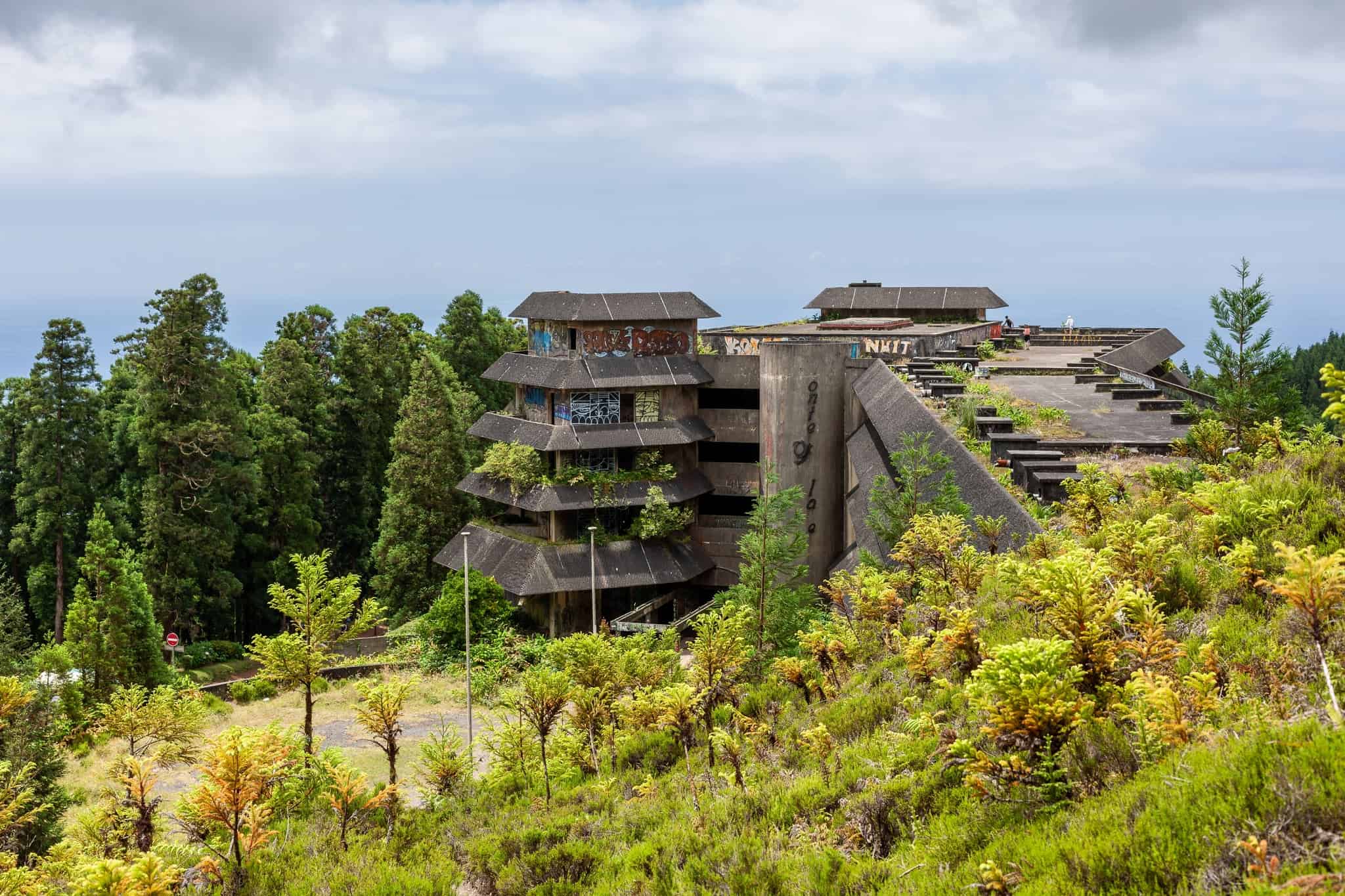 Opuštěný hotel Monte Palace zarůstající bujnou vegetací pod zamračenou oblohou, Sao Miguel, Azory